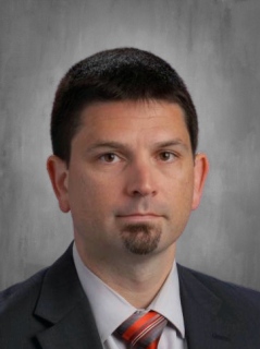 Craig Rogers is wearing a black business suit, white shirt and tie.